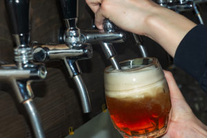 The hand of a bartender girl at a beer tap pours draft beer into a glass served in a restaurant or pub