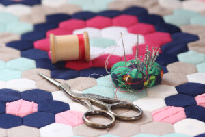 Quilting supplies on a colorful hexagon mosaic patterned quilt.